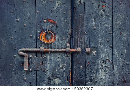 Closeup image of old wooden door with metal knob and rusty bolt.