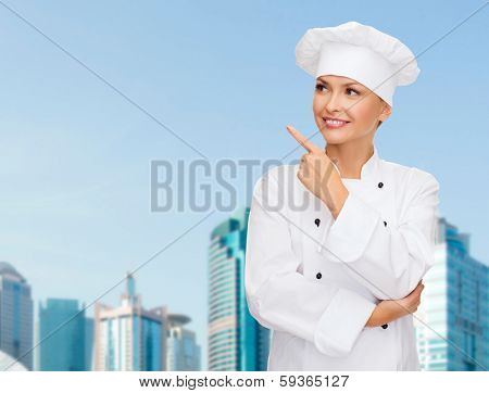cooking, advertisement and food concept - smiling female chef, cook or baker pointing finger to something