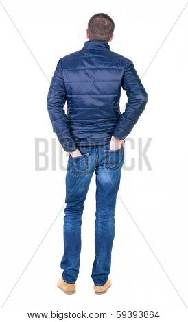 Back view of handsome man in blue windcheater looking. Standing young guy in jeans. Rear view people collection.  backside view of person.  Isolated over white background.