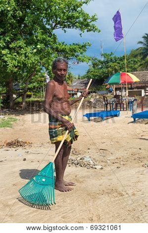 WELIGAMA, SRI LANKA - MARCH 7, 2014: Local man cleaning beach with plastic rake. Weligama is one of most popular Sri Lankan beaches,