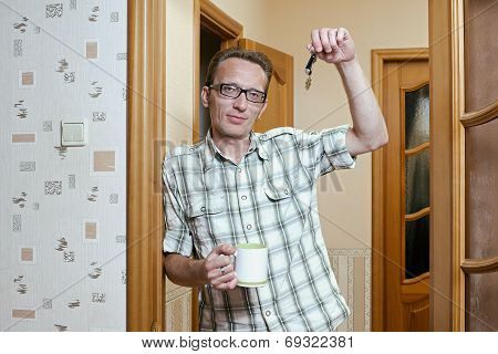Man lean the doorpost and show the keys from the new apartment.