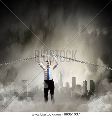 Young furious businessman breaking metal chain with hands