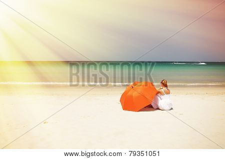 Girl with an orange umbrella on the sandy beach