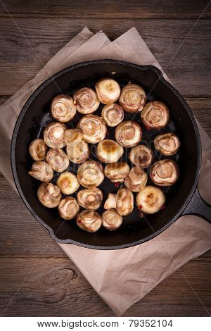 Garlic mushrooms cooked in a cast iron skillet, resting on greaseproof paper on old table. Overhead view with retro style processing.