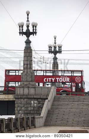 RIGA, LATVIA - MARCH 29, 2015: Red double-decker city sightseeing bus between two lanterns of Stone bridge.