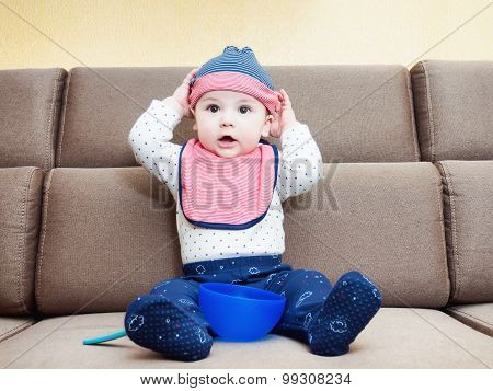 Caucasian baby boy weared bib  sitting on sofa at home