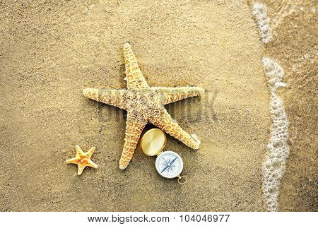 Compass with sea stars on sand beach background