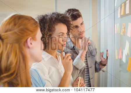 Thoughtful business poeple looking at adhesive notes on glass wall during meeting in office