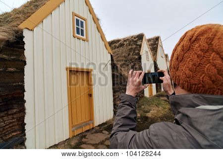 Woman taking picture with mobile cell phone of Traditional Icelandic Turf Houses in North Iceland