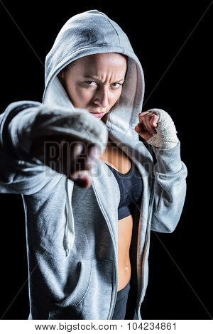 Portrait of female fighter in hood with fighting stance against black background