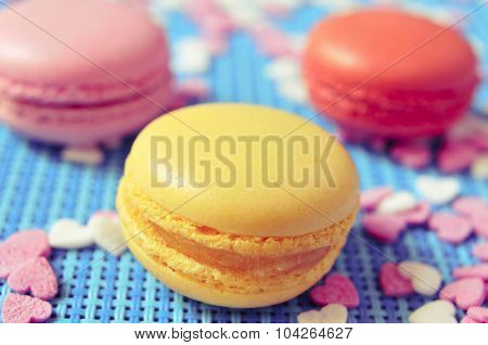 closeup some appetizing macarons with different colors and flavors on a blue tablemat with heart-shaped sprinkles