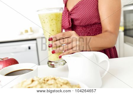 closeup of a young woman in a red dress with a glass with a smoothie in his hand, and a cup of coffee, a bowl with oatmeal cereal and a red apple on the kitchen table