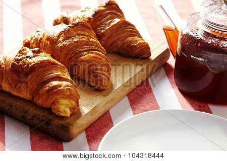 Three French Freshly Baked Croissants On Wooden Plate With Tea Pot On Striped Cloth