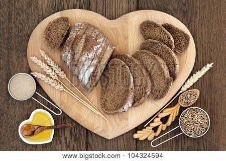 Healthy rye bread on a heart shaped board with wheat sheaths, yeast, oil, grain in love spoon and scoop over oak background.