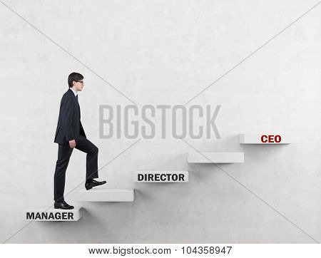 An Ambitious Man In A Suit Is Going Up The Corporate Ladder From The Manager To Ceo. Concrete Backgr