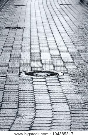 Sewer Manhole Cover On Wet Cobblestone Street