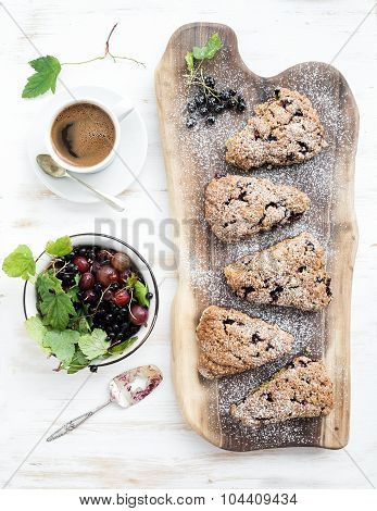 Fresh black-currant scones with coffee and bowl of berries over rustic walnut wood serving board, to