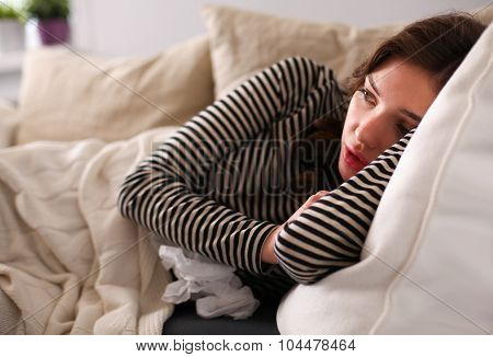 Portrait of a sick woman blowing her nose while sitting on the sofa