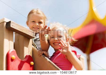 summer, childhood, leisure, friendship and people concept - happy little girls waving hands on children playground climbing frame