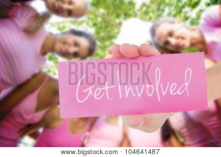The word get involved and young woman holding blank card against smiling women in pink for breast cancer awareness
