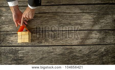 Overhead View Of Realtor Or Architect Placing A Paper Roof, Final Touch, On A Wooden  House Miniatur