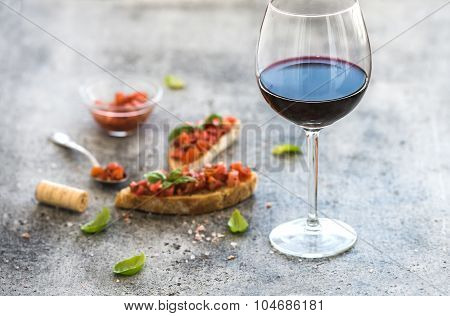 Wine appetizer set. Glass of red wine, brushettas with fresh tomato and basil on over rustic grunge