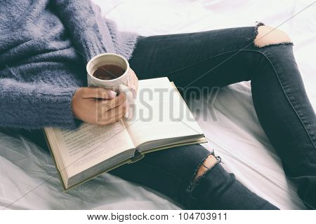 Woman on the bed with old book and cup of coffee, top view point
