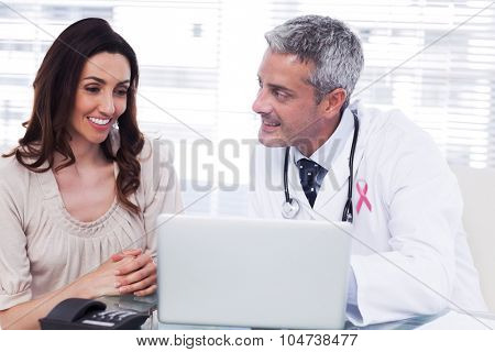 Pink awareness ribbon against docter showing something on laptop to his patient
