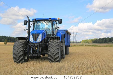 New Holland Tractor And Agricultural Trailer On Field In Autumn