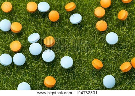 Orange and blue pills spilling on the green grass