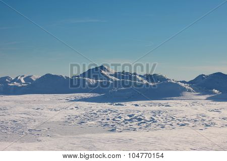 Snow desert and blue winter sky. Mountains on the horizon