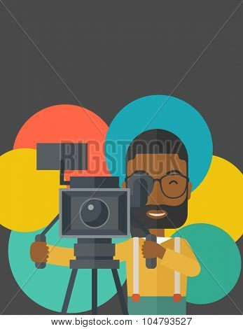 An African American cameraman with beard and glasses looking through movie camera on a tripod vector flat design illustration. Vertical layout with a text space.