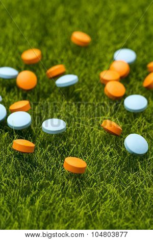 Orange and blue round pills spilling on the green grass