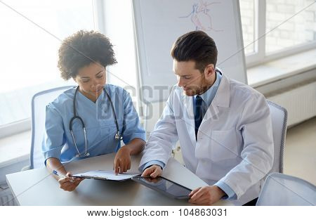 health care, people, technology and medicine concept - doctor and nurse with tablet pc computer and clipboard meeting and discussing something at hospital