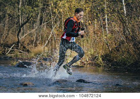 Young man runner splash water in river, during crossing a mountain river