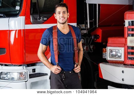 Portrait of smiling young fireman standing against firetrucks at station