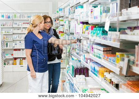 Female pharmacist removing product for customer from shelf in pharmacy