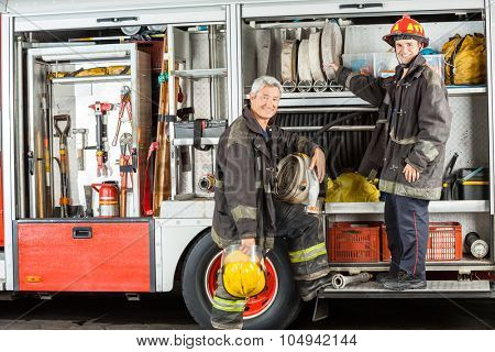 Portrait of confident male firefighters standing on truck at fire station