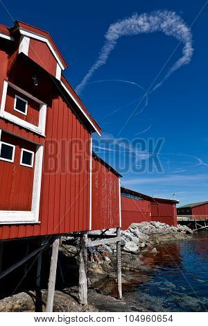 Summer Norwegian Landscape with a red wooden fisherman cabin and blue sky and clouds