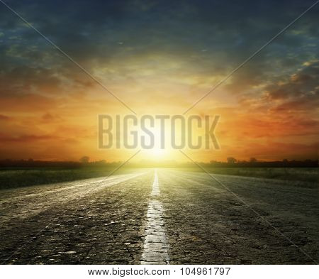 Long country road with white lines down the centre stretching off past a lone tree to the distant horizon 