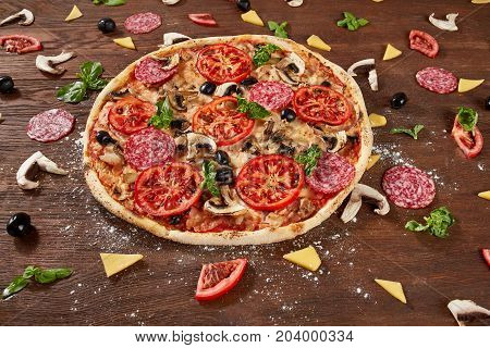 Pizza with tomatoes, mozzarella cheese, black olives and basil. Delicious italian pizza on wooden pizza board. Table top view