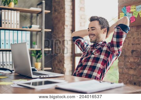Cheerful Young Brunet Guy Is Watching At His Laptop Screen, At His Work Place, With Arms Behind The