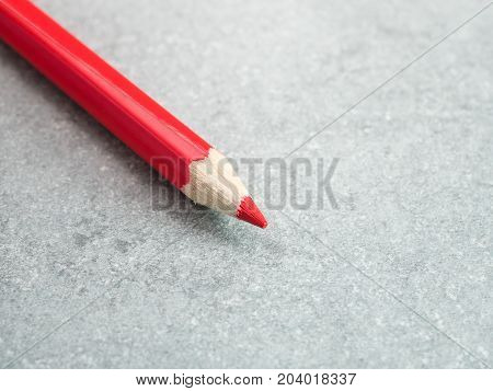 Closeup red color pencil on bare cement or concrete wall background (Selective Focus)