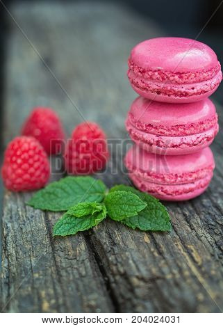 Delicious macarons raspberry flavored with fresh raspberries and a sprig of mint presented on a wooden shelf
