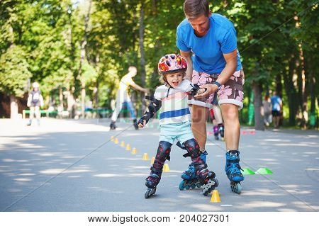 Portait of cute baby boy with inline skating instructor in the park learining to skate.