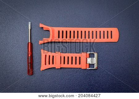 Orange watchband rubber skin & repairing tool kit for adjusting watchband on isolated blue background.