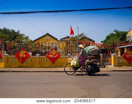 HOIAN, VIETNAM, SEPTEMBER, 04 2017: Unidentified woman biking in the street view with old houses, and colorful lanters made of paper, in Hoi An ancient town, UNESCO world heritage. Hoi An is one of the most popular destinations in Vietnam.