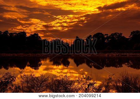 Sky And Rays Of Sunlight With Sun Reflections Above Silhouettes Of Trees And Lake.
