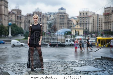 Blonde wooman dreesed in black dress in the city. Rainy day. Autumn in Kyiv