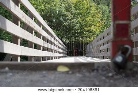 With a lock pad locked across the bridge. The bridge is in focus. In the background are trees.